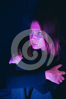 Portrait of a sad young woman with star makeup, illuminated by the pink light of a nightclub. Melancholy at a party. Loneliness