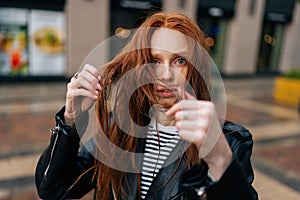 Portrait of sad young woman touching wet hair after autumn rain standing on beautiful city street, looking at camera.