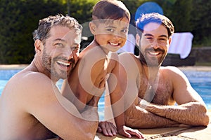 Portrait Of Same Sex Family With Two Dads And Son On Holiday In Swimming Pool Together