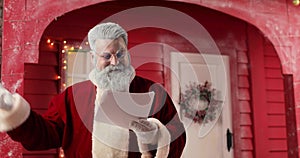 Portrait of Santa Claus, amazedly and laughingly reading letters in a beautiful New Year's decorated studio against the