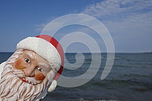 Portrait of Santa Claus. Christmas by the sea. Christmas garden gnome with Santa hat looks around the corner  on vacation in the t