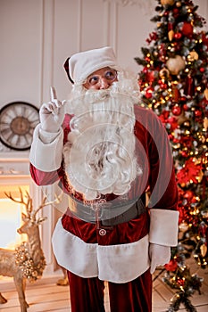 Portrait of Santa Claus with glasses near the fireplace and christmas tree with gifts. New year and Merry Christmas , happy