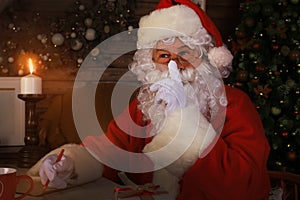 Portrait of Santa Claus keeping forefinger by his mouth and looking at camera