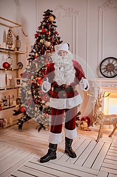 Portrait of Santa Claus showing thumb up near the fireplace and christmas tree with gifts. New year and Merry Christmas , happy