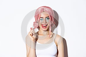 Portrait of sassy attractive girl in pink wig, wearing outfit for halloween party, smiling and winking at camera