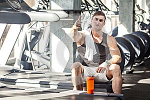 Portrait of satisfied athlete handsome masculine man sitting during treadmill exercise in gym, tired sportsman drinking water in