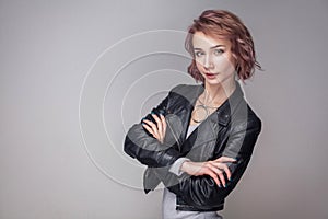 Portrait of satisfied beautiful happy girl with short hair and makeup in casual style black leather jacket standing crosed hands