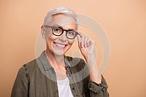 Portrait of satisfied business woman wearing khaki shirt touch eyeglases new style accessories advert isolated on beige