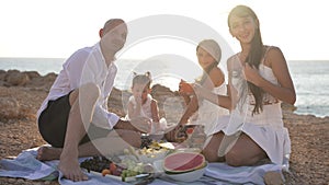 Portrait of satisfied Caucasian father and daughters posing in sunbeam outdoors on picnic on sea coast. Smiling handsome