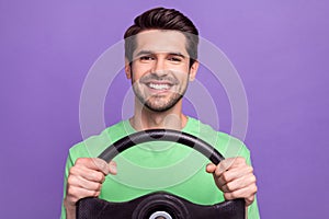 Portrait of satisfied cheerful guy with bristle wear green t-shirt holding steering wheel driving car isolated on violet