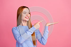 Portrait of satisfied girl with foxy hair wear blue pullover look directing at offer on palm empty space isolated on