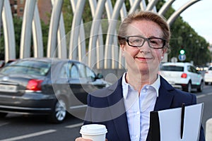 A portrait of a satisfied looking business woman with holding to go cup of coffee, documents folder and pen