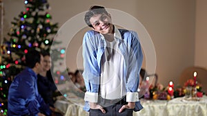 Portrait satisfied Middle Eastern teenage boy looking at camera smiling standing in living room with blurred family