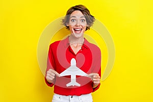 Portrait of satisfied positive gorgeous girl with bob hairdo dressed red shirt hold white paper plane isolated on yellow