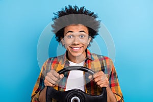 Portrait of satisfied positive guy with perming coiffure dressed plaid shirt hands hold steering wheel isolated on blue