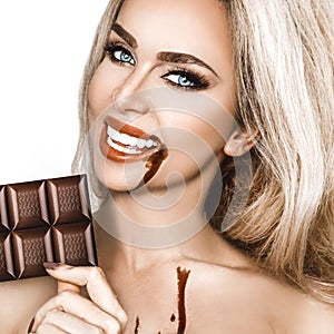 Portrait of a satisfied pretty girl biting chocolate bar and looking at camera isolated over white background. Close-up shot of