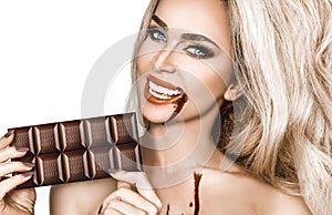 Portrait of a satisfied pretty girl biting chocolate bar and looking at camera isolated over white background. Close-up shot of