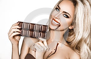 Portrait of a satisfied pretty girl biting chocolate bar and looking at camera isolated over white background. Close-up shot of