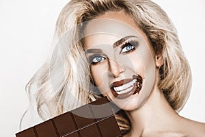 Portrait of a satisfied pretty girl biting chocolate bar and looking at camera isolated over white background. Close-up shot of