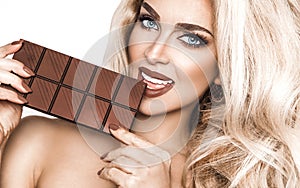 Portrait of a satisfied pretty girl biting chocolate bar and looking at camera isolated over white background. Close-up shot of