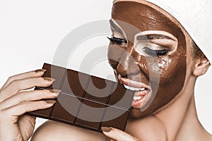 Portrait of a satisfied pretty girl biting chocolate bar and looking at camera isolated over white background. Close-up shot of