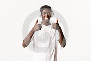 Portrait of satisfied, smiling african-american guy enjoying awesome music, showing thumbs-up in approval, listening