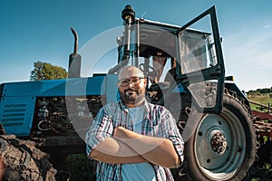 Portrait of satisfied tractor driver after work on agricultural field stands next to tractor. Farming and harvesting