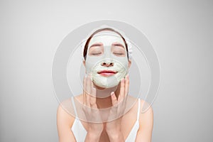 Portrait of satisfied woman improves her skin condition, wears facial mask, touches cheeks over white background photo