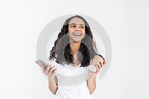 Portrait of a satisfied young woman using mobile phone while holding cup of coffee to go over white background