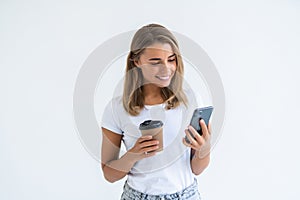 Portrait of a satisfied young woman using mobile phone while holding cup of coffee to go isolated over white background
