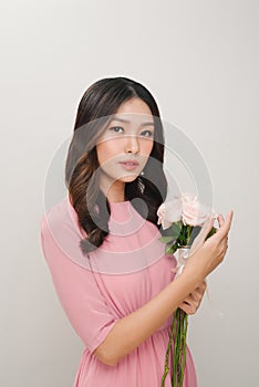 Portrait of a satisfied young woman dressed in pink dress holding bouquet of roses isolated over white background