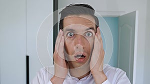 Portrait of scared businessman looks into camera with startle at face clutches his head showing fear and panic. Shocked