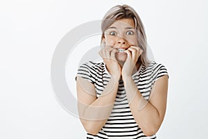 Portrait of scared cute insecure woman with blond hair and braces, biting fingernails and staring with fright at camera