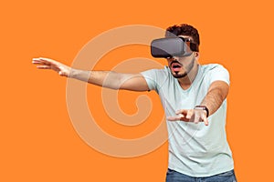 Portrait of scared gamer, brunette man stretching arms forward while playing virtual reality game. isolated on orange background