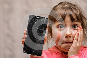 Portrait of a scared little girl with a broken mobile phone. A sad child broke the screen of a mobile phone. Cracked display in