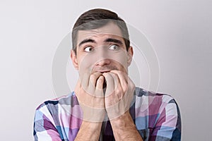 Portrait of scared man biting his nails isolated on grey background