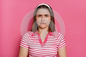 Portrait of scared nervous young Caucasian woman wearing striped T-shirt and hair band posing isolated over pink background,