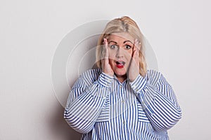 Portrait of a scared overweight woman in studio, hands on cheeks.