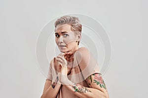 Portrait of scared tattooed woman with pierced nose and short hair in beige t shirt looking cowered, terrified isolated