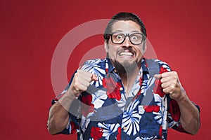 Portrait of a scared young man in Hawaiian shirt against red background.