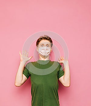 Portrait of scared young man in medical mask with raised up in fear looking at camera with shocked eyes, isolated on pink. Fear of
