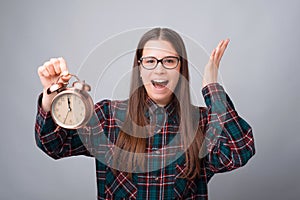 Portrait of scared young woman holding alarm clock over grey backgorund