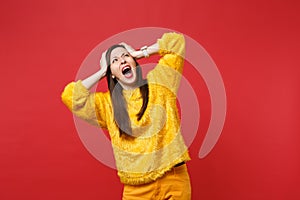 Portrait of scared young woman in yellow fur sweater screaming, looking up, clinging to head isolated on bright red