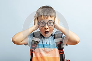 Portrait of school boy in glasses with funny shocked face expression isolated on blue background. Back to school