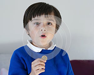 Portrait school kid showing one pound coin on his hand with proud face after back from school, Child boy wearing school uniform ho