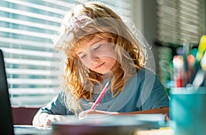 Portrait school kid siting on table doing homework. Concentrated serious child writing in notebook. Focused schoolboy