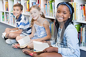 Portrait of school kids sitting on floor and reading book in library