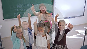 Portrait of school kids with teacher showing thumbs up and then applaud in classroom on background of board at school