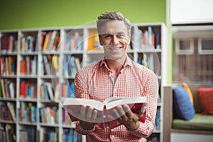 Portrait of school teacher holding book in library