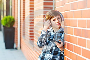 Portrait of schoolboy boy with modern hairstyle hair. Guy listens to music or watches video from his smart phone. New generation